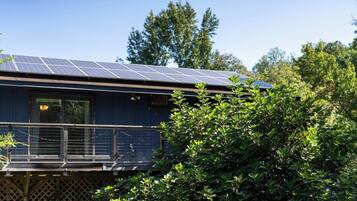 A house with a solar panel roof, a balcony, and dense greenery in the foreground.