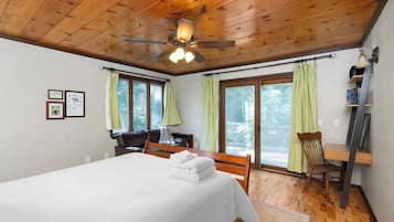 Une chambre à coucher comprenant un lit, un bureau, une chaise, un ventilateur de plafond et de grandes fenêtres avec des rideaux.
