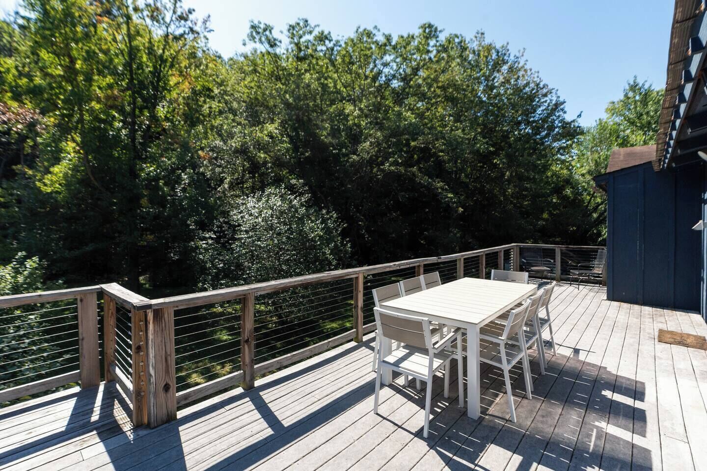 Un terrazzo in legno con tavolo e sedie, circondato da una ringhiera metallica, con vista su una zona boschiva.