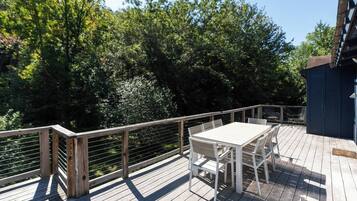 Un terrazzo in legno con tavolo e sedie, circondato da una ringhiera metallica, con vista su una zona boschiva.