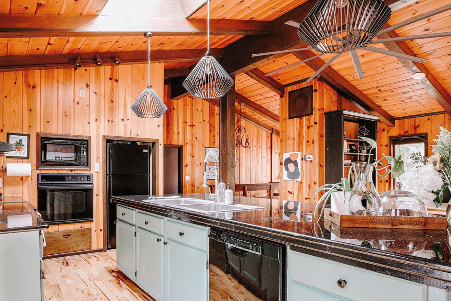 Une cuisine aux murs et au plafond en bois, avec des luminaires suspendus.