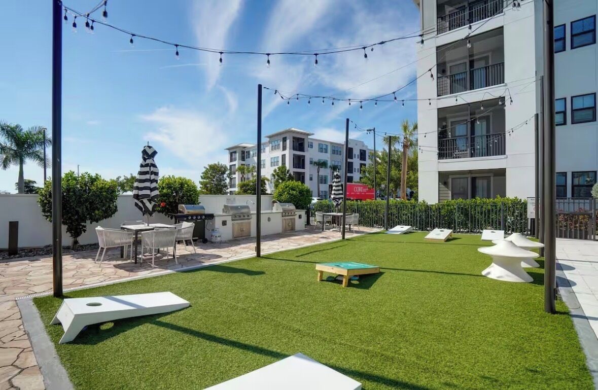 A courtyard with artificial grass, outdoor seating, a barbecue area, and a building with balconies.