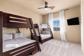 Ein Schlafzimmer mit zwei Etagenbetten, einem Deckenventilator, einem an der Wand montierten Fernseher und einem Fenster mit Vorhängen.