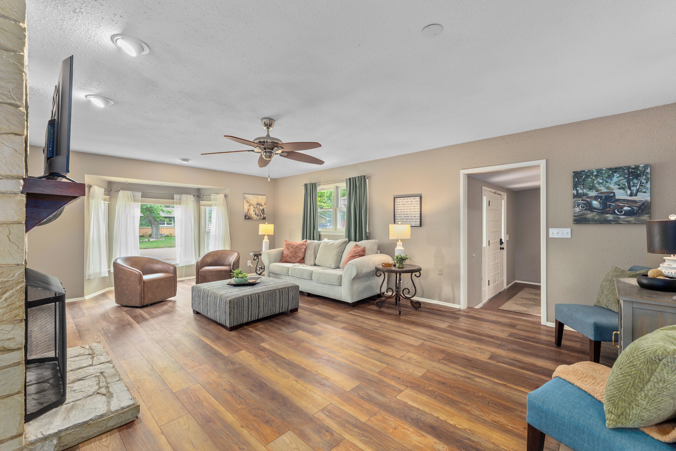 A spacious living room with hardwood flooring, a ceiling fan, a fireplace, and a television mounted on the wall.