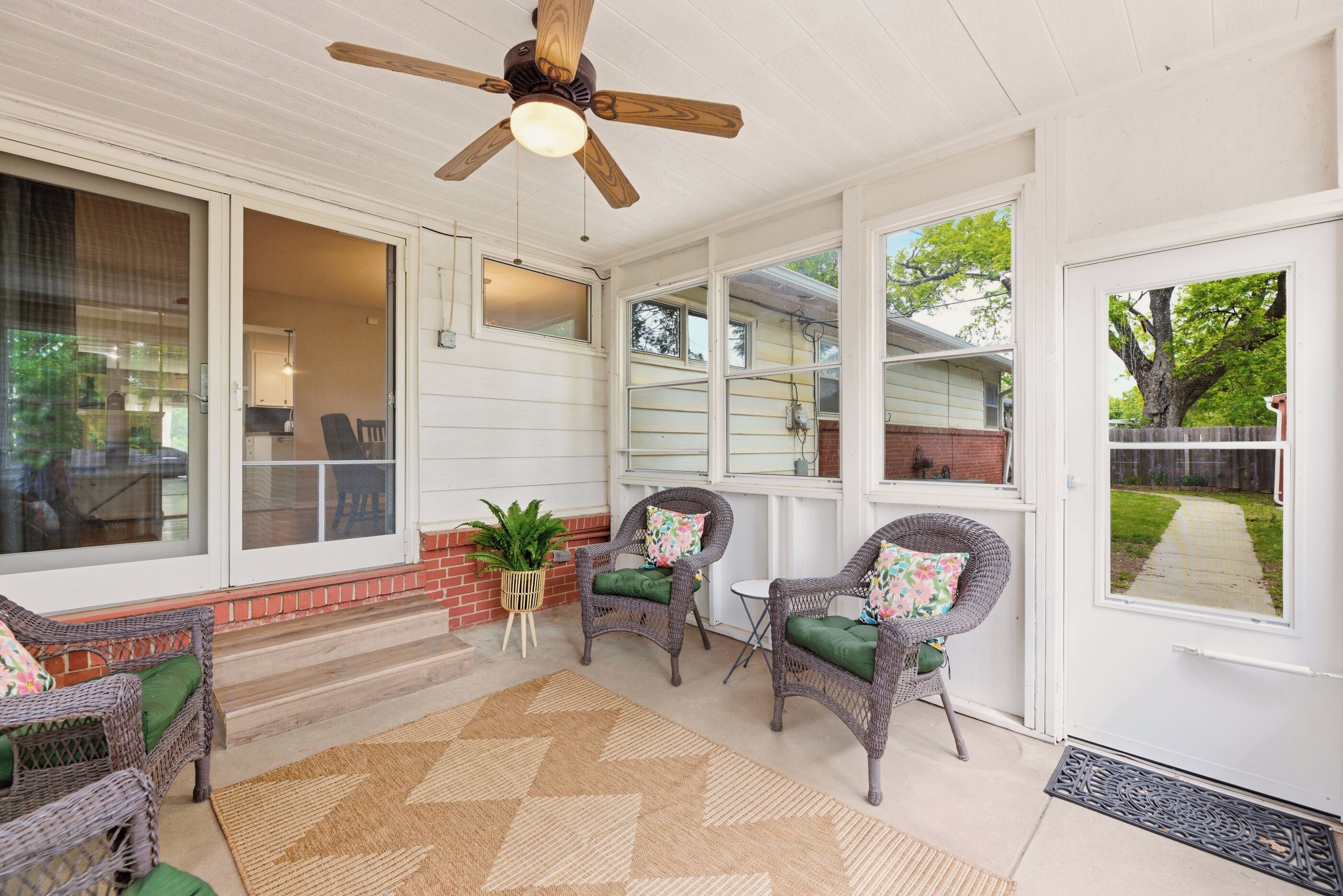 A covered porch with wicker furniture, a ceiling fan, and large windows.