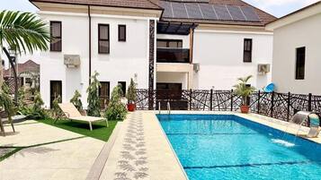 A residential building with a swimming pool, solar panels on the roof, and a fenced patio area.
