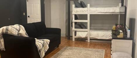 A room with a bunk bed, a black sofa, a small table, and a wicker basket.