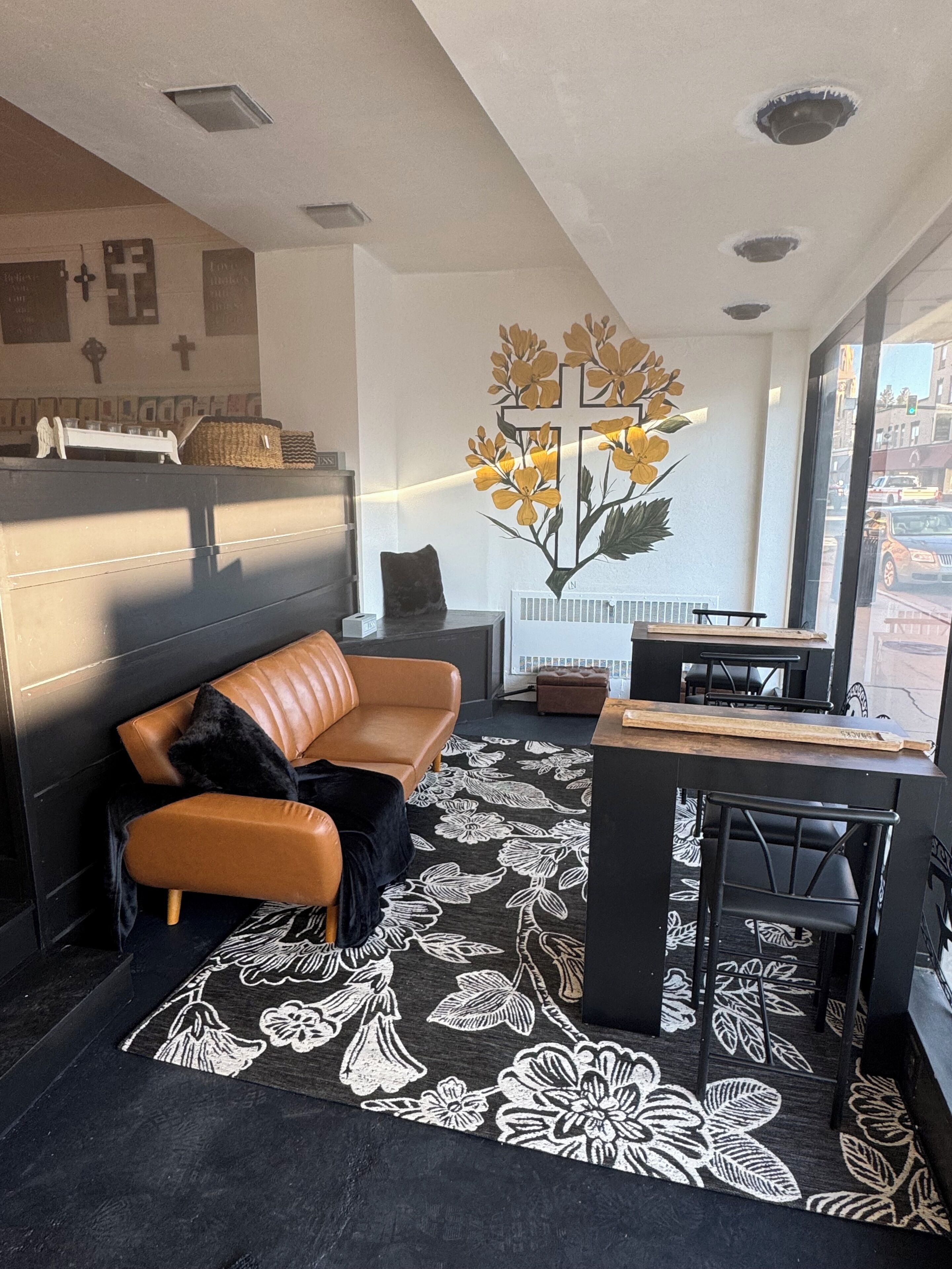 A modern living room with a leather sofa, a coffee table, and a large window offering a view of the street.