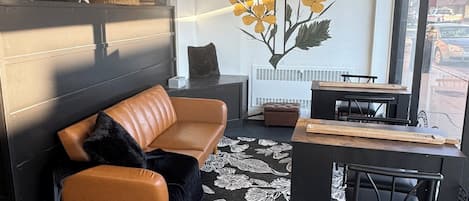A modern living room with a leather sofa, a coffee table, and a large window offering a view of the street.