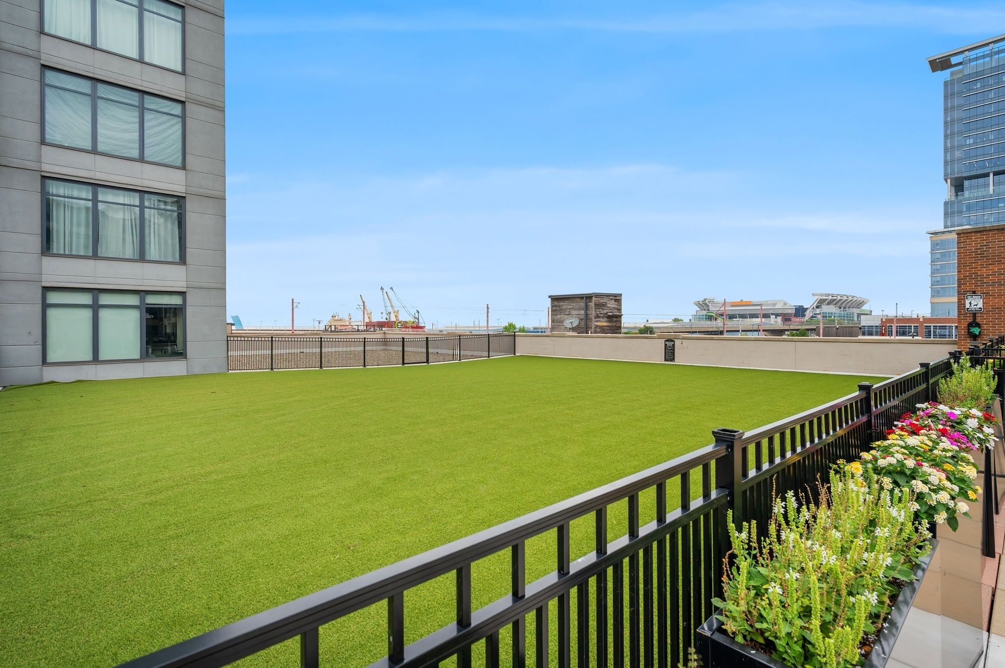 A rooftop with artificial grass, a metal fence, and a row of potted plants.