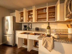Una cocina con un refrigerador de acero inoxidable, armarios abiertos con vajilla, una botella de vino y un microondas.