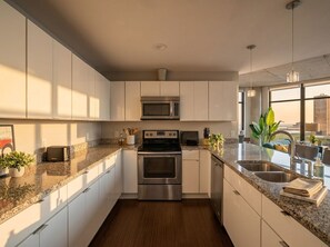 A modern kitchen with white cabinets, a stainless steel oven, a microwave, and a granite countertop. - Flats DT + Balcony + Dog Park + On-site Parking (Cleveland)