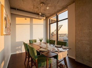 A dining area with a large window, a table set for four, and a view of a bridge. - Flats DT + Balcony + Dog Park + On-site Parking (Cleveland)