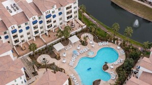Ein Hotel mit Schwimmbad, umgeben von Liegestühlen und Palmen.