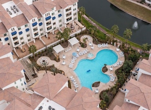 A hotel with a swimming pool surrounded by lounge chairs and palm trees.