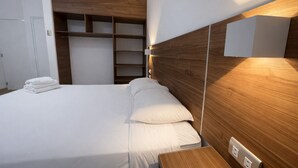 Una habitación de hotel moderna con una cama bien hecha, cabecera de madera, armario empotrado y mesita de noche con lámpara.