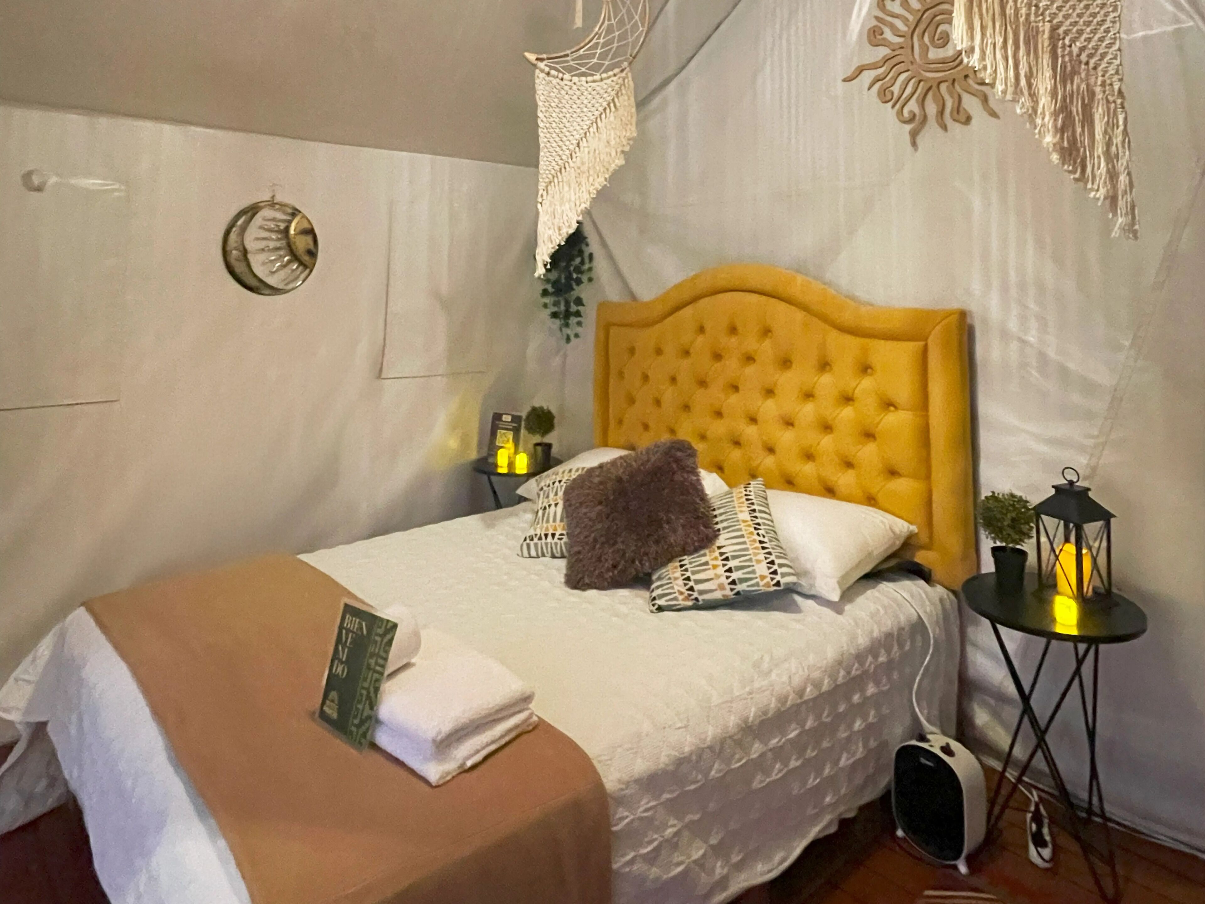 A neatly made bed with a yellow headboard, a bedside table with a lamp, and a small potted plant.