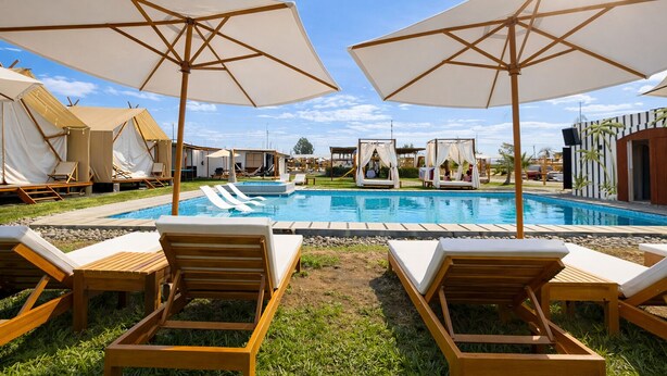 Un área de piscina con sillones de descanso y sombrillas, carpas y una piscina.