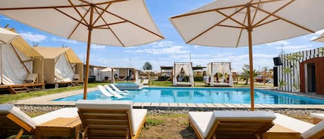 A pool area with lounge chairs and umbrellas, tents, and a pool.