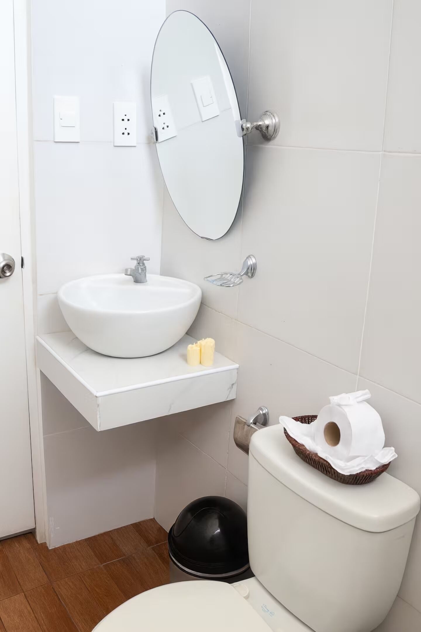 A bathroom with a white sink, a mirror, a toilet, and a black trash bin.