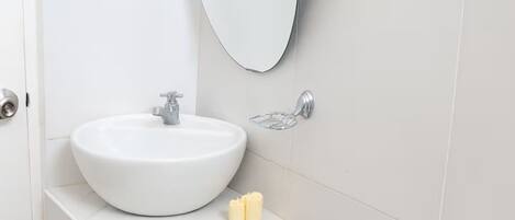 A bathroom with a white sink, a mirror, a toilet, and a black trash bin.