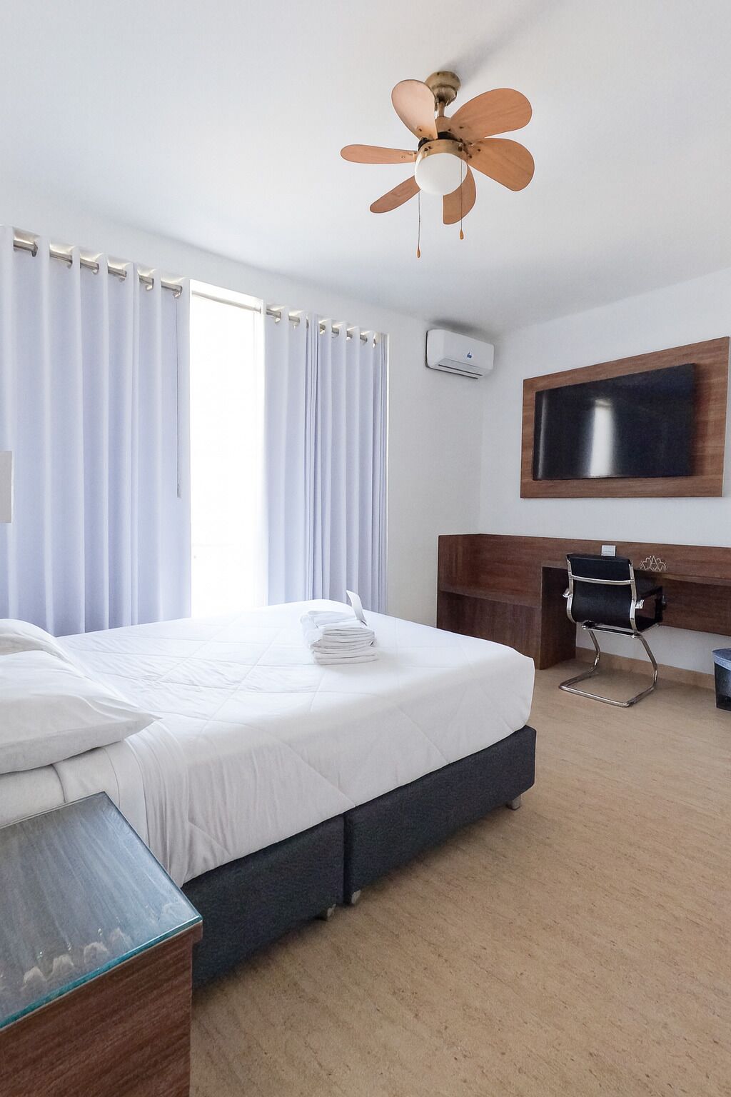 Une chambre d’hôtel équipée d’un lit, d’un bureau, d’une chaise, d’une télévision et d’un ventilateur de plafond.