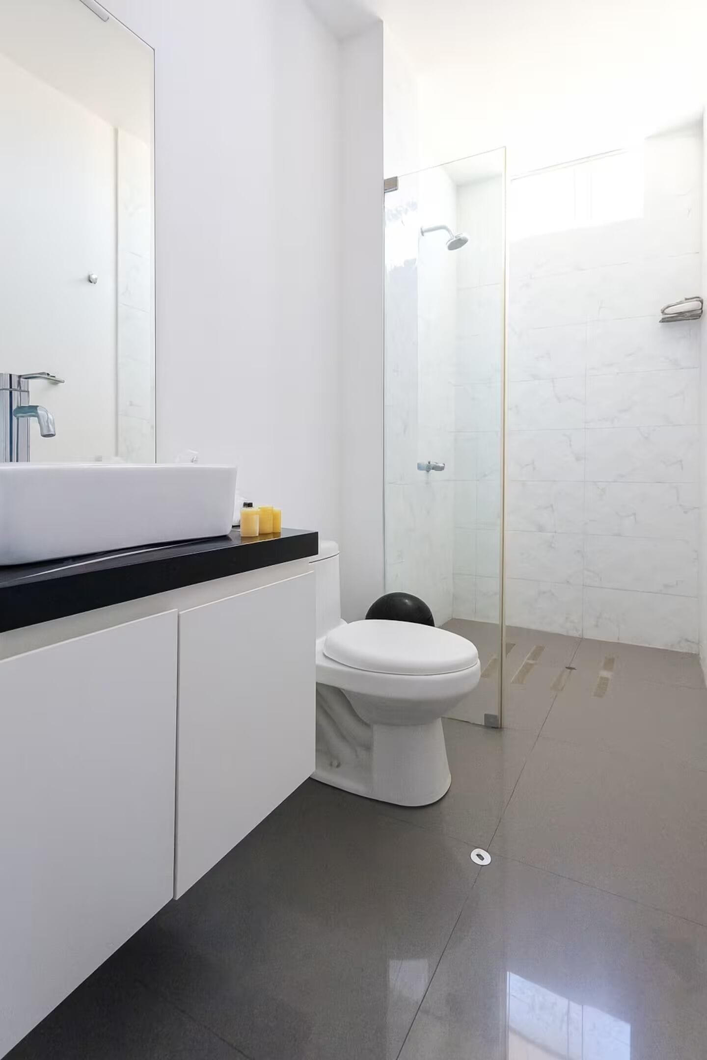Ein modernes Badezimmer mit Toilette, einer Duschkabine aus Glas und einem großen Spiegel über dem Waschbecken.