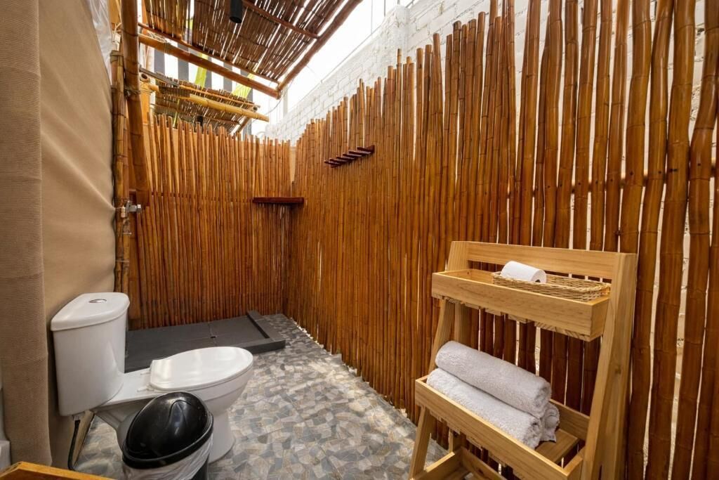 Baño pequeño y funcional con pared de bambú, inodoro, lavamanos y estante de madera con toallas.