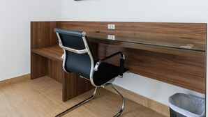 Un espacio de oficina moderno con un escritorio de madera, una silla de oficina negra, un televisor montado y un equipo de aire acondicionado.