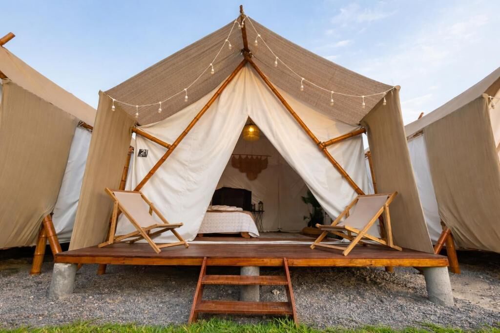 Una carpa con plataforma de madera, una cama y dos sillas.