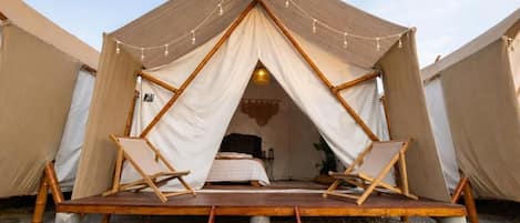 A tent with a wooden deck, a bed, and two chairs.
