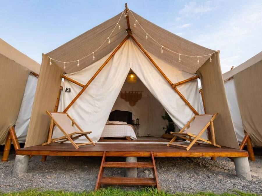 Una tenda amb un terra de fusta, un llit i dues cadires.