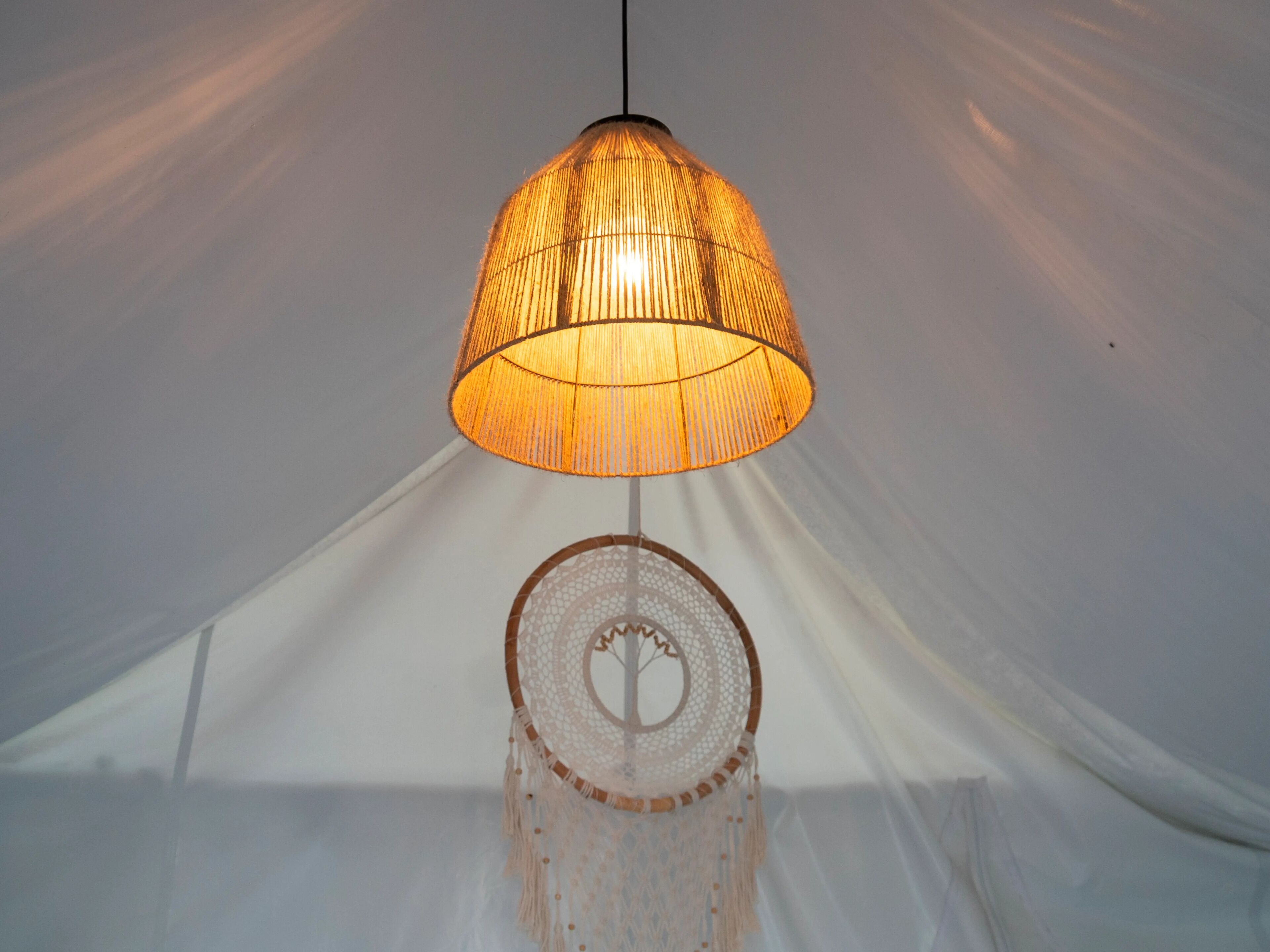 A hanging lamp with a woven shade and a macrame wall hanging below it.