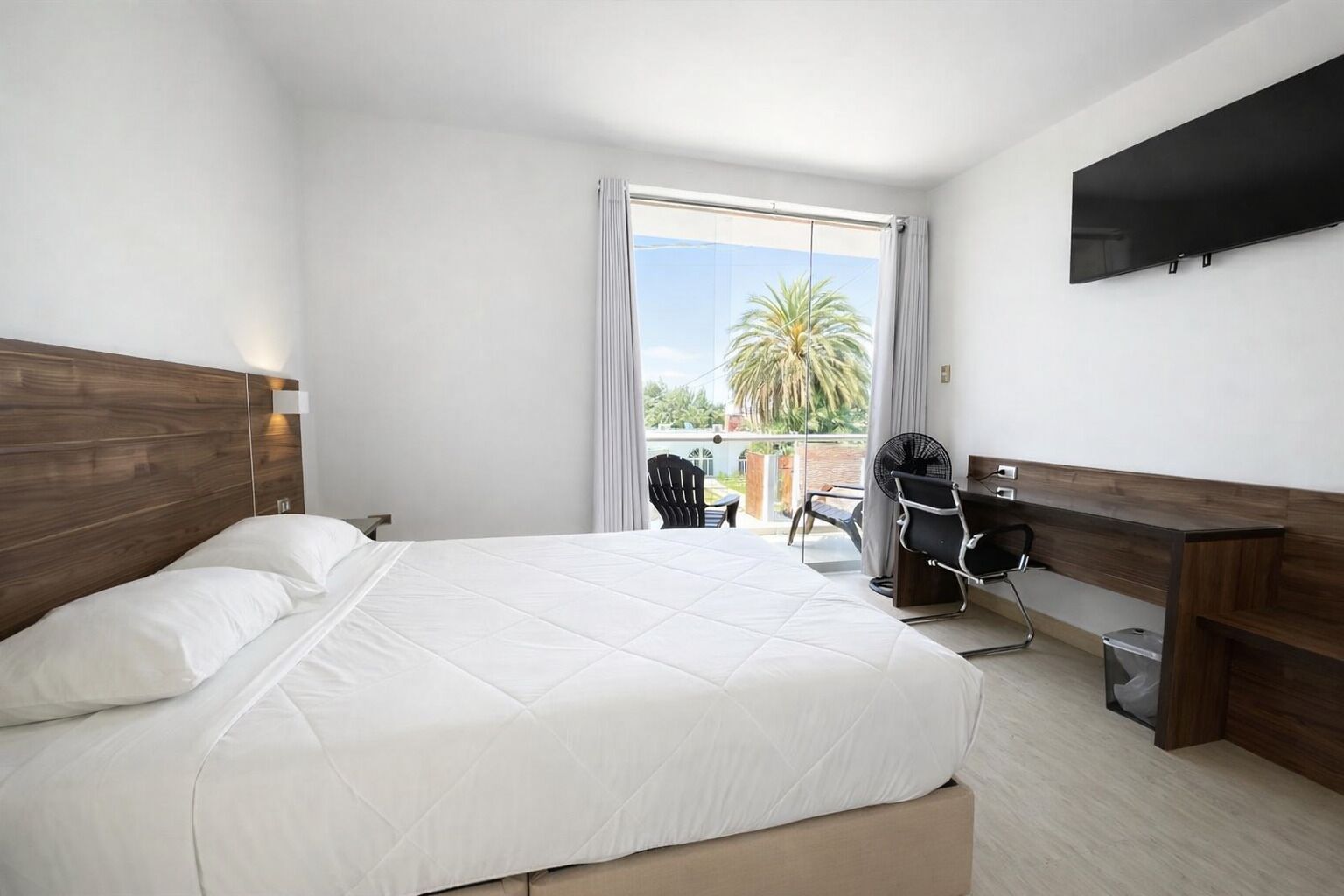 A hotel room with a bed, a desk, a chair, and a TV mounted on the wall.