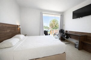 Una habitación de hotel con cama, escritorio, silla y televisor montado en la pared.