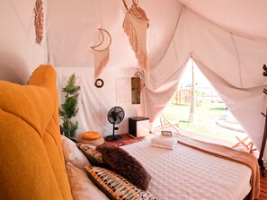 Una tienda de campaña con cama, ventilador y vistas al exterior.