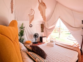 Una tienda de campaña con cama, ventilador y vistas al exterior.