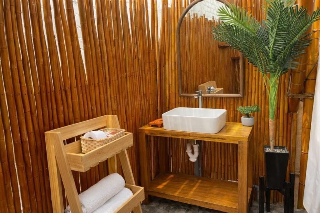 Un baño con pared de madera, un lavamanos blanco, un espejo, una repisa con toallas y una planta en maceta.