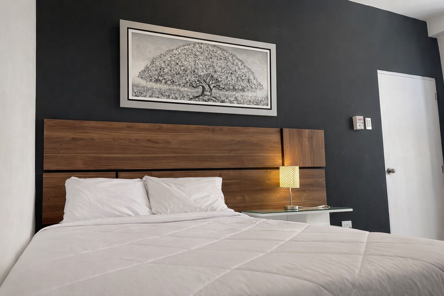 Un dormitorio con cama, mesita de noche, lámpara y un cuadro en la pared.