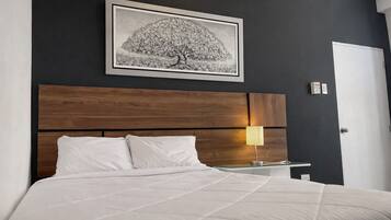 Un dormitorio con cama, mesita de noche, lámpara y un cuadro en la pared.