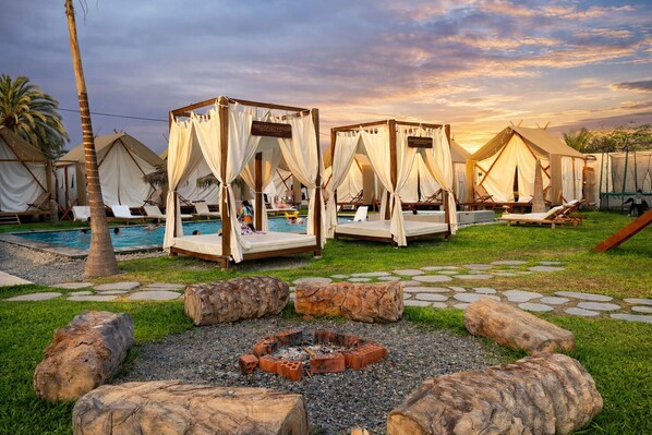 Un resort con varias tiendas de campaña, una piscina y un brasero rodeado de rocas.