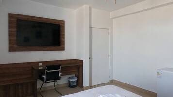 A hotel room with a bed, a desk, a television mounted on the wall, and a ceiling fan.