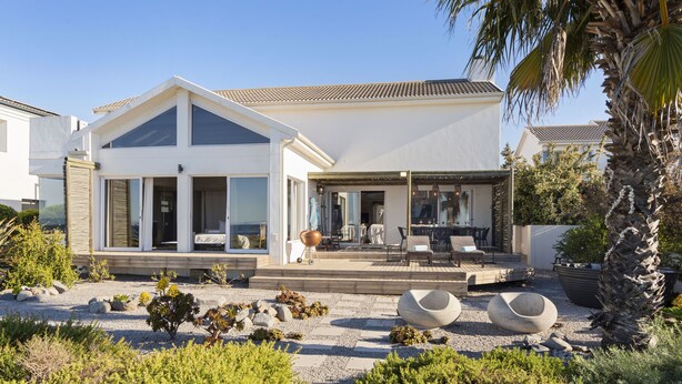 Een modern huis met een ruim terras, tuinmeubilair buiten en een verzorgde tuin.