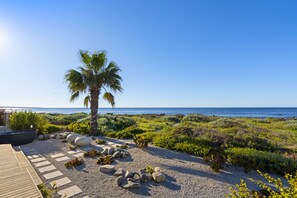 Ein Küstengarten mit einer Palme, felsigem Gelände und Blick auf das Meer.