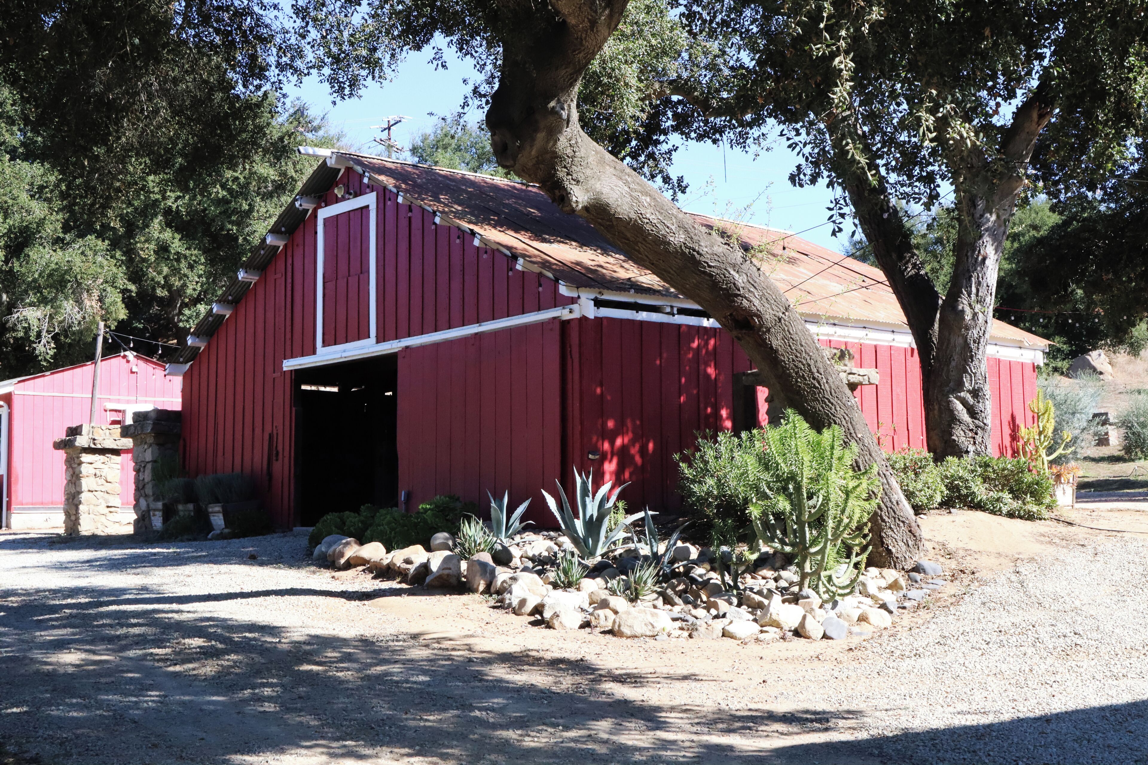 Une grange rouge avec une allée en terre battue et un jardin de rocaille.
