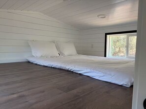 Ein Schlafzimmer mit einem Bett, Holzboden und einem Fenster.