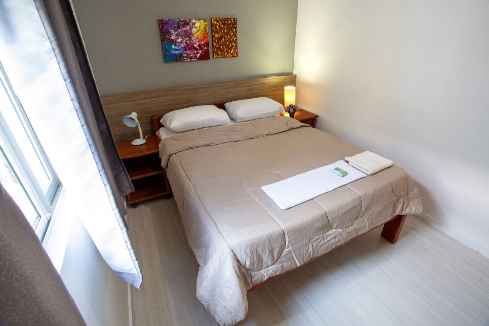 A hotel room with a bed, bedside tables, a lamp, and artwork on the wall.