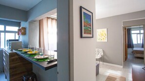 A modern kitchen with a dining area, a white chair, and a bed in the adjacent room. - StayHome Florianópolis - 6 Hóspedes  (Florianópolis)