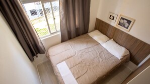 Una cama con cabecera de madera, una ventana con cortinas y dos cuadros en la pared.