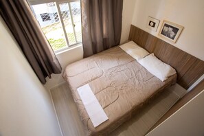 A bed with a wooden headboard, a window with curtains, and two framed pictures on the wall. - StayHome Florianópolis - 6 Hóspedes  (Florianópolis)